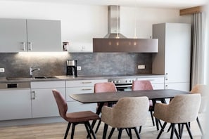 A modern kitchen with a dining area, featuring a stainless steel range hood, a coffee machine, and a set of chairs. - Holiday apartment in Riezlern with Wi-Fi (Riezlern)