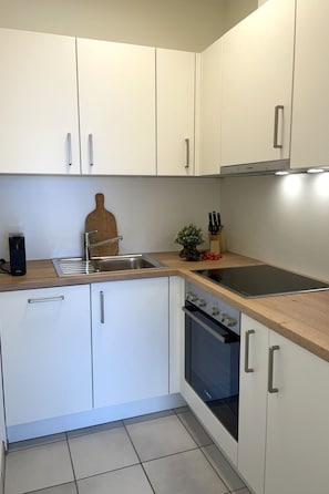 A compact kitchen with white cabinets, a stainless steel sink, a wooden cutting board, a small potted plant, and a knife block. - Azzurro by Interhome (Minusio)