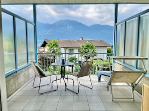 A balcony with a view of mountains, a table with chairs, and a hammock. - Azzurro by Interhome (Minusio)