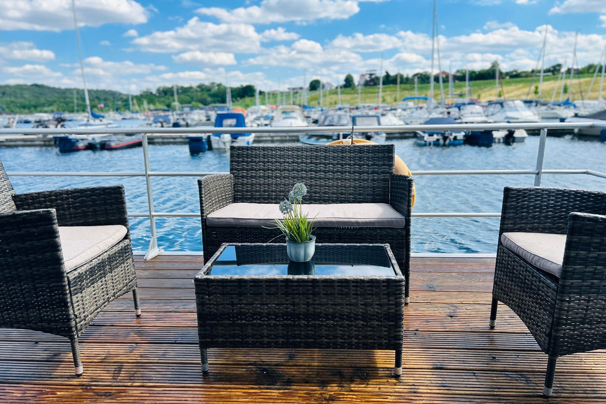 Eine Terrasse mit Korbmöbeln und einem Glastisch mit Blick auf eine Marina und Boote.