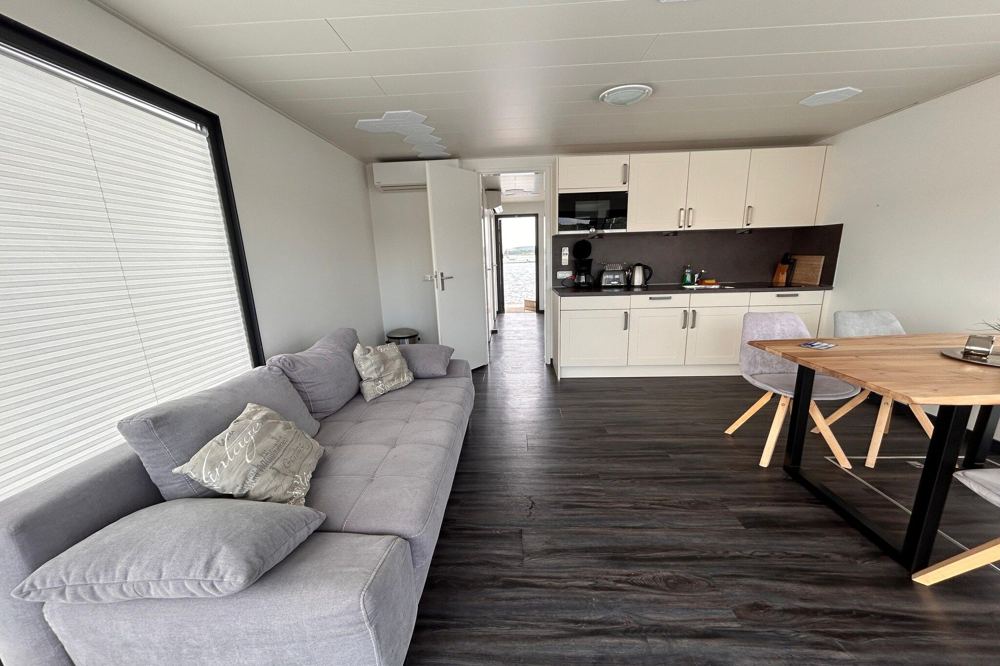 Ein modernes Interieur mit einem grauen Sofa, einem Holzesstisch und einer Küchenzeile.