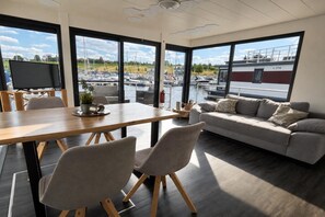 A modern interior with a dining area, sofa, and large windows overlooking a marina. - Houseboat with roof terrace on Lake Geiseltal (Braunsbedra)