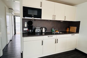 A modern kitchen with white cabinetry, a black countertop, a Siemens microwave, a coffee maker, and a kettle. - Houseboat with roof terrace on Lake Geiseltal (Braunsbedra)