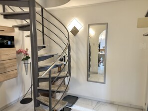 Eine Wendeltreppe mit Metallgeländer, ein Blumentopf und ein Spiegel, der einen Küchenbereich reflektiert.