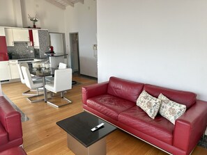 A modern living room with a red leather sofa, a black coffee table, and a dining area with a white table and chairs. - Residenza Delphin by Interhome (Brissago)