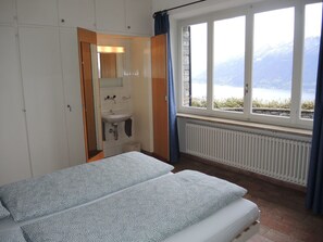 A bedroom with a bed, a bathroom with a sink, and a window with a view of mountains. - La Civetta by Interhome (Brissago)