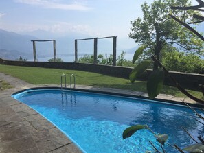 Ein Schwimmbecken mit einer Steindeck, Metallleitern und Blick auf Berge im Hintergrund.