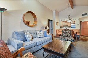 A living room with a sofa, a coffee table, a chair, a round mirror, and a kitchen area with wooden cabinets and a hanging light fixture. - 2BR villa with kitchen, pool, hot tub & resort access in Midway.3054-2 (Midway)