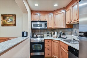 A modern kitchen with wooden cabinets, stainless steel appliances, granite countertops, and a painting on the wall. - 2BR villa with kitchen, pool, hot tub & resort access in Midway.3054-2 (Midway)