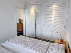 A bedroom with a bed, a dresser, a mirror, and a closet with sliding doors. - Apartment Siesta by Interhome (San Nazzaro)