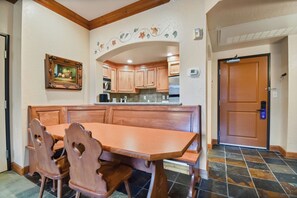 Uma área de refeições com mesa e cadeiras de madeira, uma cozinha ao fundo e uma porta com tranca de segurança.