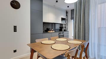 Une cuisine moderne avec des meubles de couleur grise, une table à manger en bois et des sets de table en fibres tressées, ainsi qu’une horloge noire accrochée au mur.