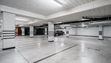 Un parking à plusieurs niveaux, avec des piliers en béton, une voiture garée dans l’une des places et un éclairage au plafond.