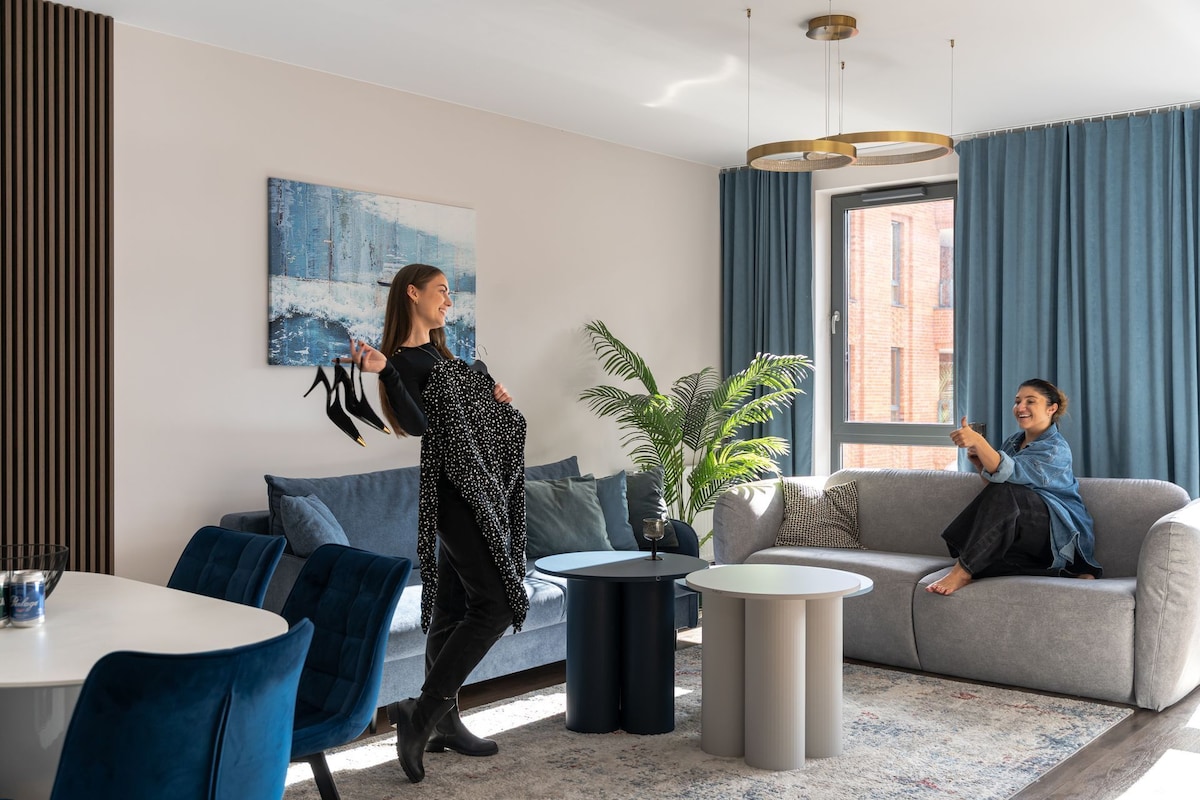 Een moderne woonkamer met een bank, een salontafel, een eettafel met stoelen en een groot raam met gordijnen.