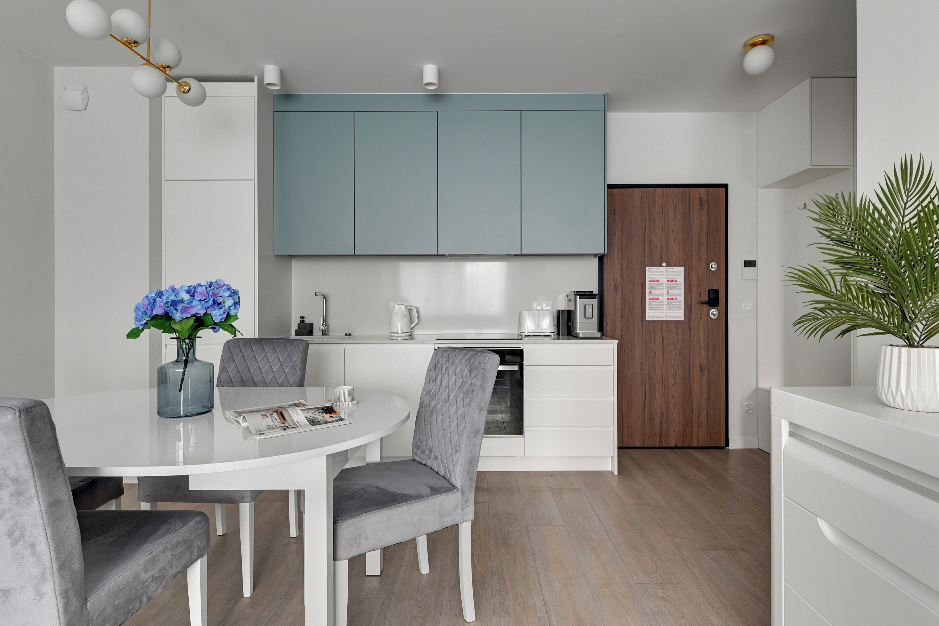 A modern kitchen with white cabinets, a wooden door, and a dining area with a table and chairs.