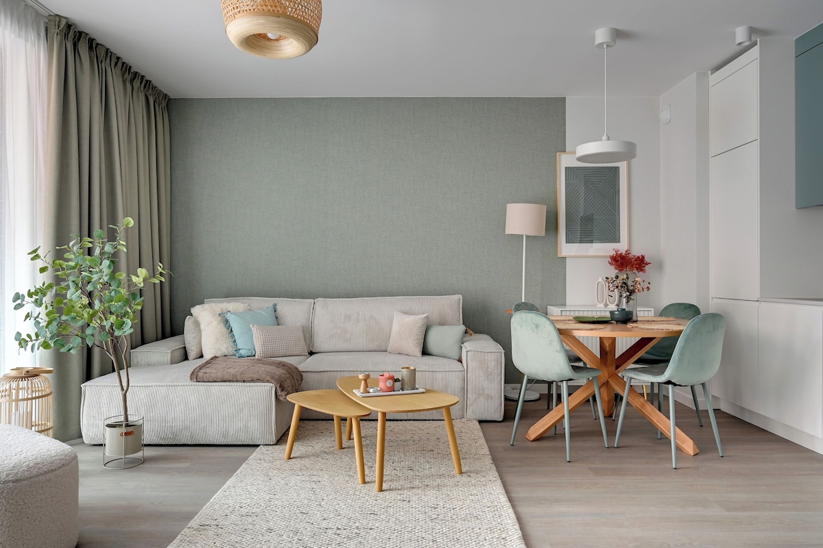 Een moderne woonkamer met een bank, een eettafel met stoelen, een hanglamp en een plant.