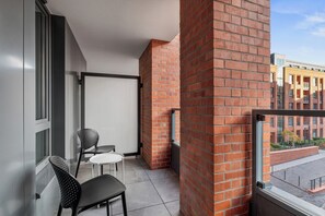 Een balkon met een bakstenen muur, een deur met metalen frame, twee stoelen en een kleine tafel.
