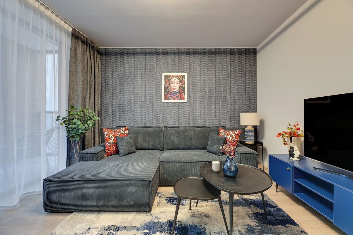 Een moderne woonkamer met een hoekbank, een salontafel, een televisie en een decoratieve wand.