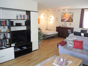 A modern living room with a flat-screen TV, bookshelves, a sofa, a dining table, and a painting on the wall. - Attico Monte Carlo by Interhome (Brissago)