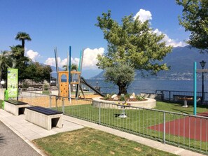 A playground with a slide, swings, and a climbing structure, surrounded by a fence and a bench. - Attico Monte Carlo by Interhome (Brissago)