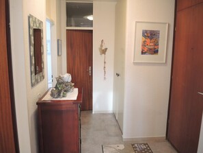 A hallway with a wooden door, a mirror, a small table with decorative items, and a framed picture on the wall. - Attico Monte Carlo by Interhome (Brissago)