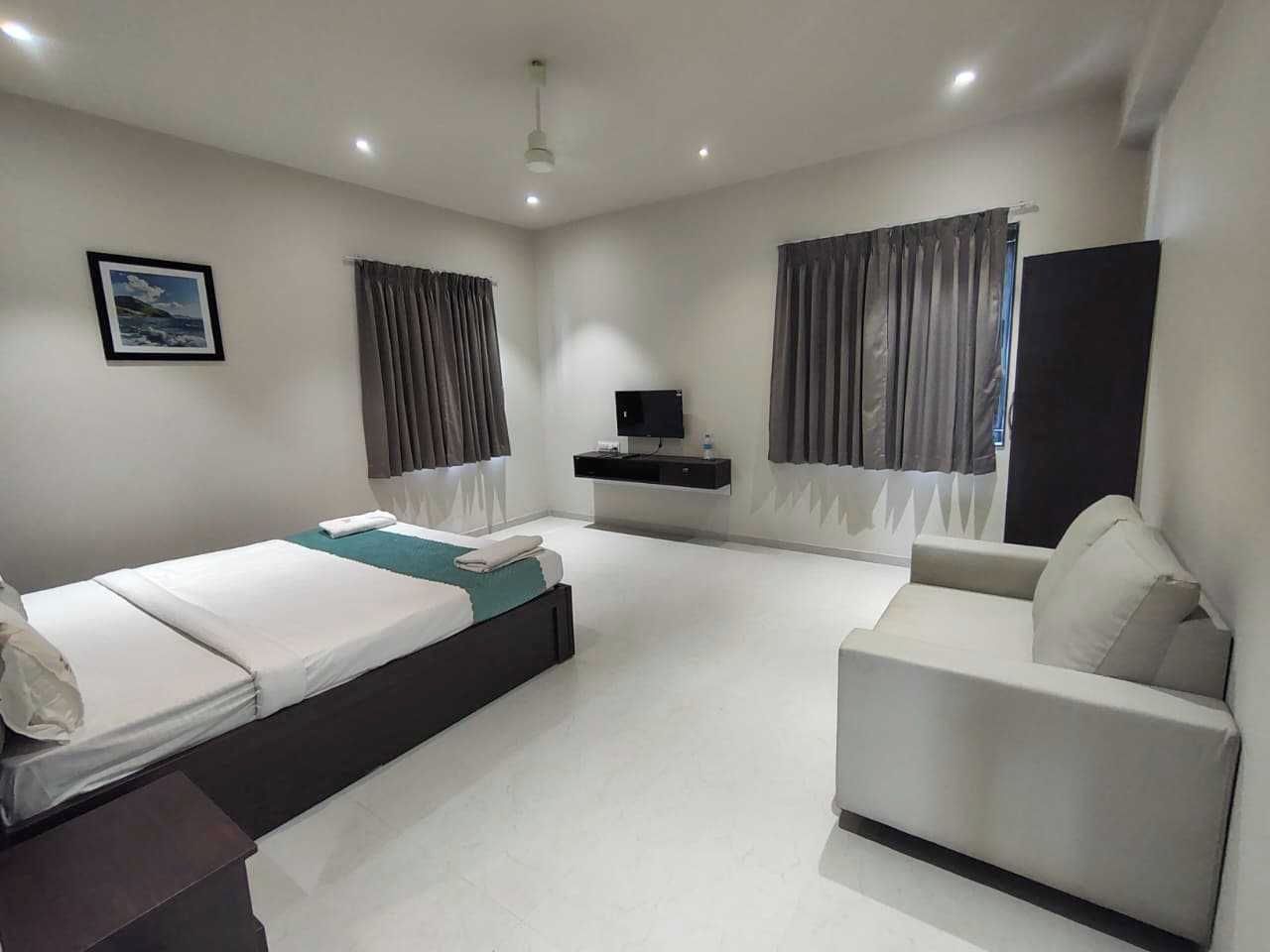 Una habitación de hotel moderna con cama, sofá, televisor y ventana con cortinas.