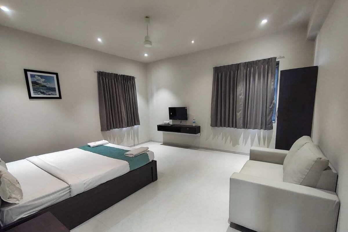 Una habitación de hotel moderna con cama, sofá, televisor y ventana con cortinas.