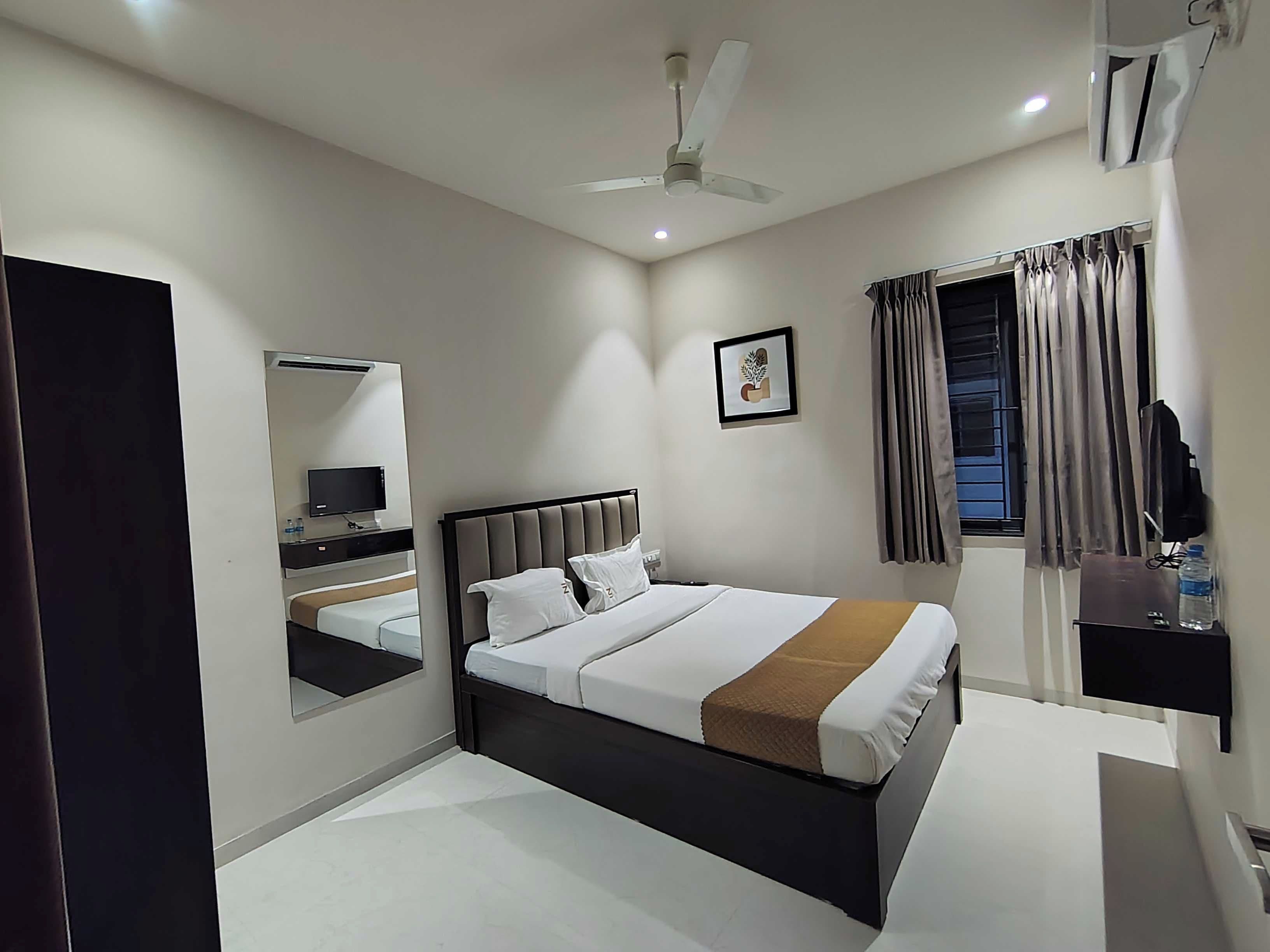 A modern hotel room with a bed, a TV, a desk, and a ceiling fan.