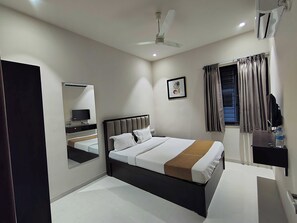 A modern hotel room with a bed, a TV, a desk, and a ceiling fan.