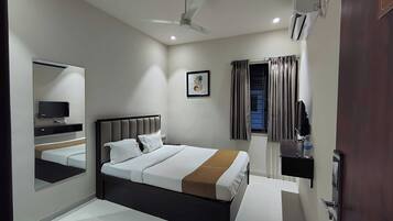 Habitación de hotel con cama, televisor, ventilador de techo, ventana con cortinas y puerta.