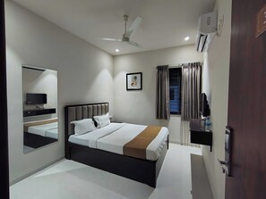 Habitación de hotel con cama, televisor, ventilador de techo, ventana con cortinas y puerta.