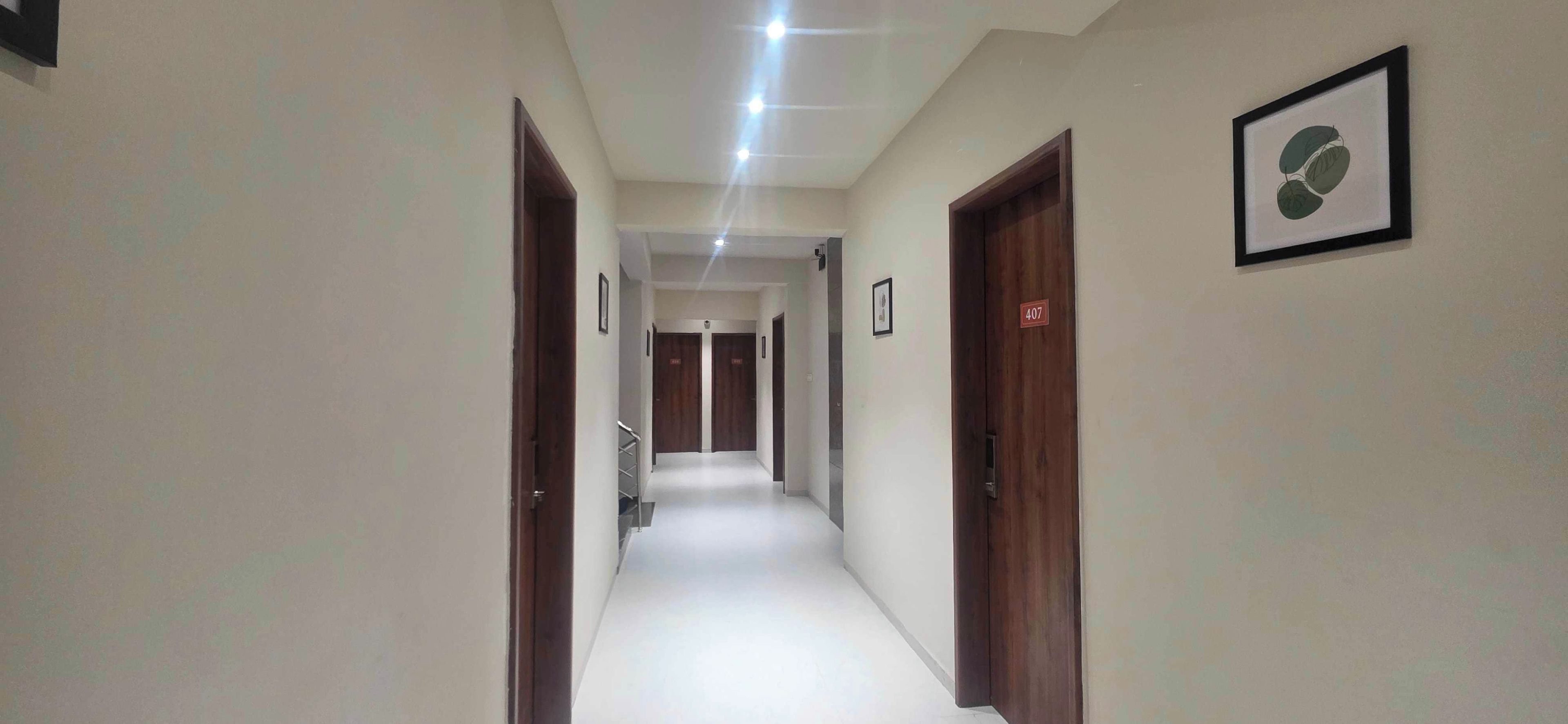 Un pasillo con puertas a ambos lados, una escalera al final y un cartel con número en una puerta.