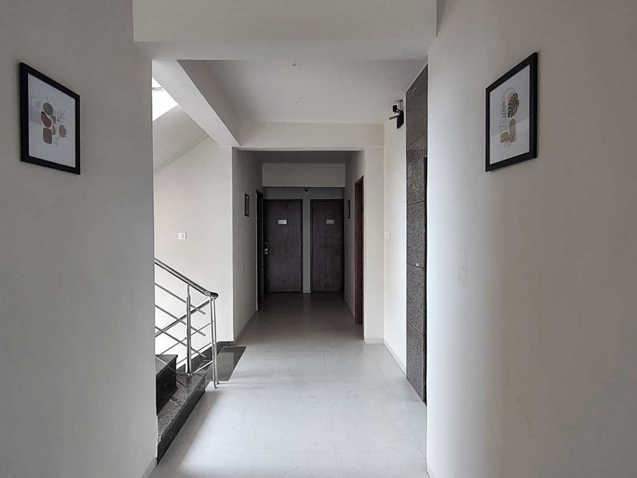 A hallway with a staircase on the left, a door at the end, and framed pictures on the walls.