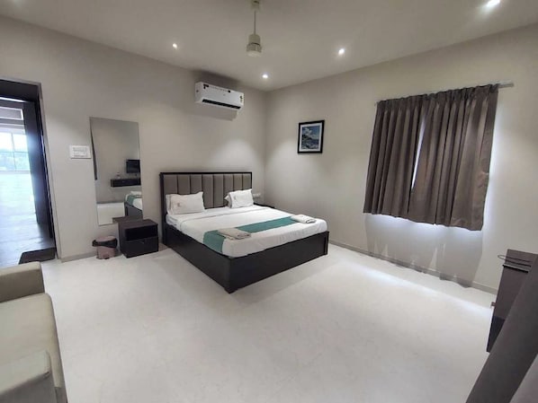 A modern hotel room with a large bed, a bedside table, a mirror, an air conditioning unit, and a window with curtains.