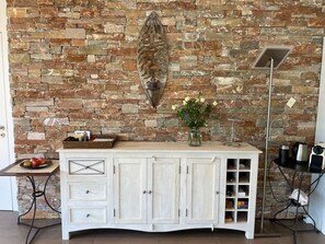 A kitchen with a stone wall, a white cabinet with drawers, a vase with flowers, and a floor lamp. - Luxury Apartment by Interhome (Minusio)