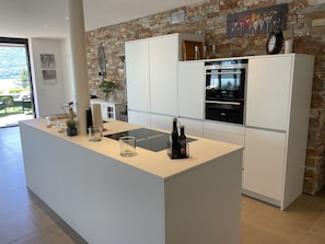 A modern kitchen with a central island, white cabinetry, a stone accent wall, and a view of the outdoors. - Luxury Apartment by Interhome (Minusio)