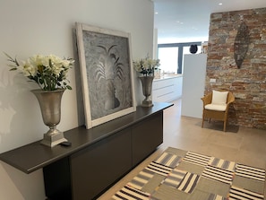 A modern interior with a dark-toned console table, two large vases with white flowers, a framed abstract artwork, a patterned rug, and a stone wall. - Luxury Apartment by Interhome (Minusio)