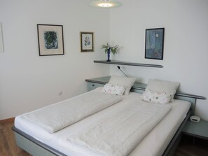 A double bed with a white bedspread and matching pillows, a bedside table with a lamp, and two framed artworks on the wall. - Casa Lydia by Interhome (Brione sopra Minusio)