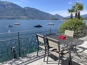 A terrace with a table and chairs overlooking a lake with boats, mountains, and a clear sky. - Villa Genovese by Interhome (Minusio)