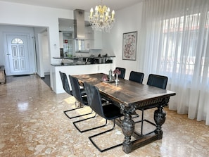 A dining area with a marble floor, a wooden table with chairs, a chandelier, and a kitchen in the background. - Villa Genovese by Interhome (Minusio)