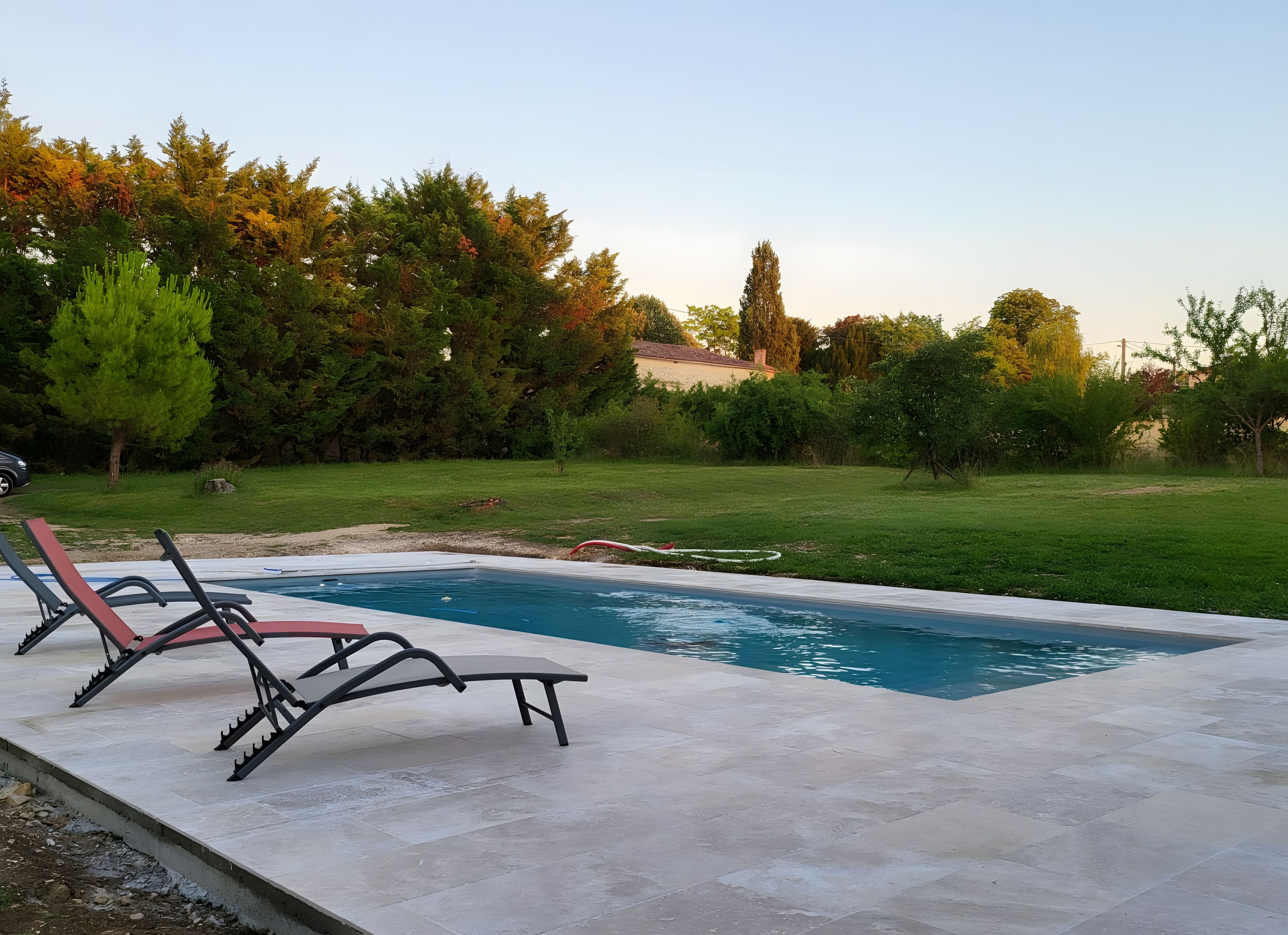 A swimming pool with lounge chairs and a grassy area with trees.