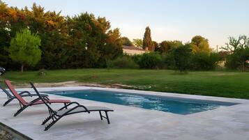 A swimming pool with lounge chairs and a grassy area with trees.