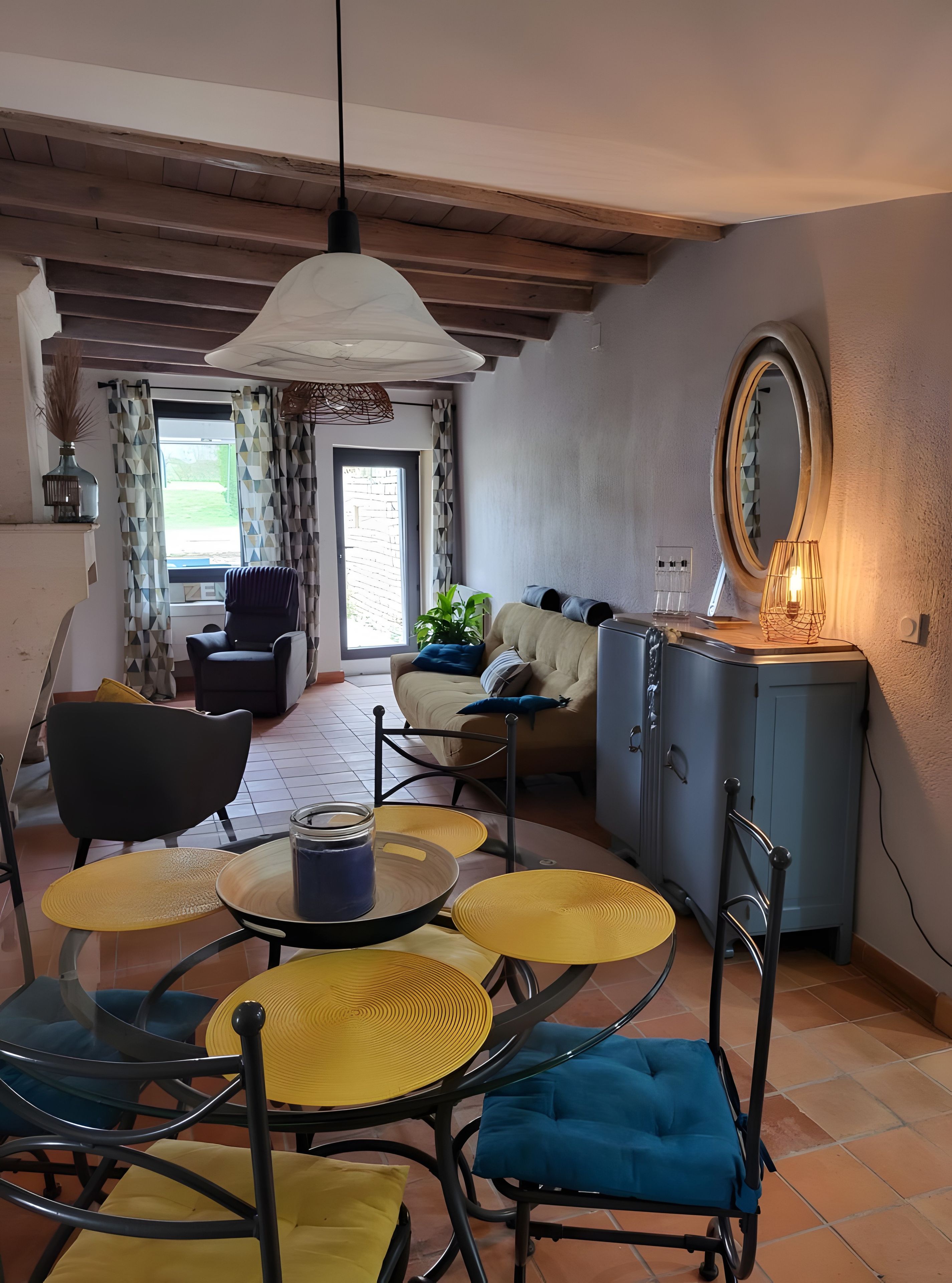Un salon comprenant un coin repas, un canapé, un fauteuil, un meuble et une fenêtre avec des rideaux.