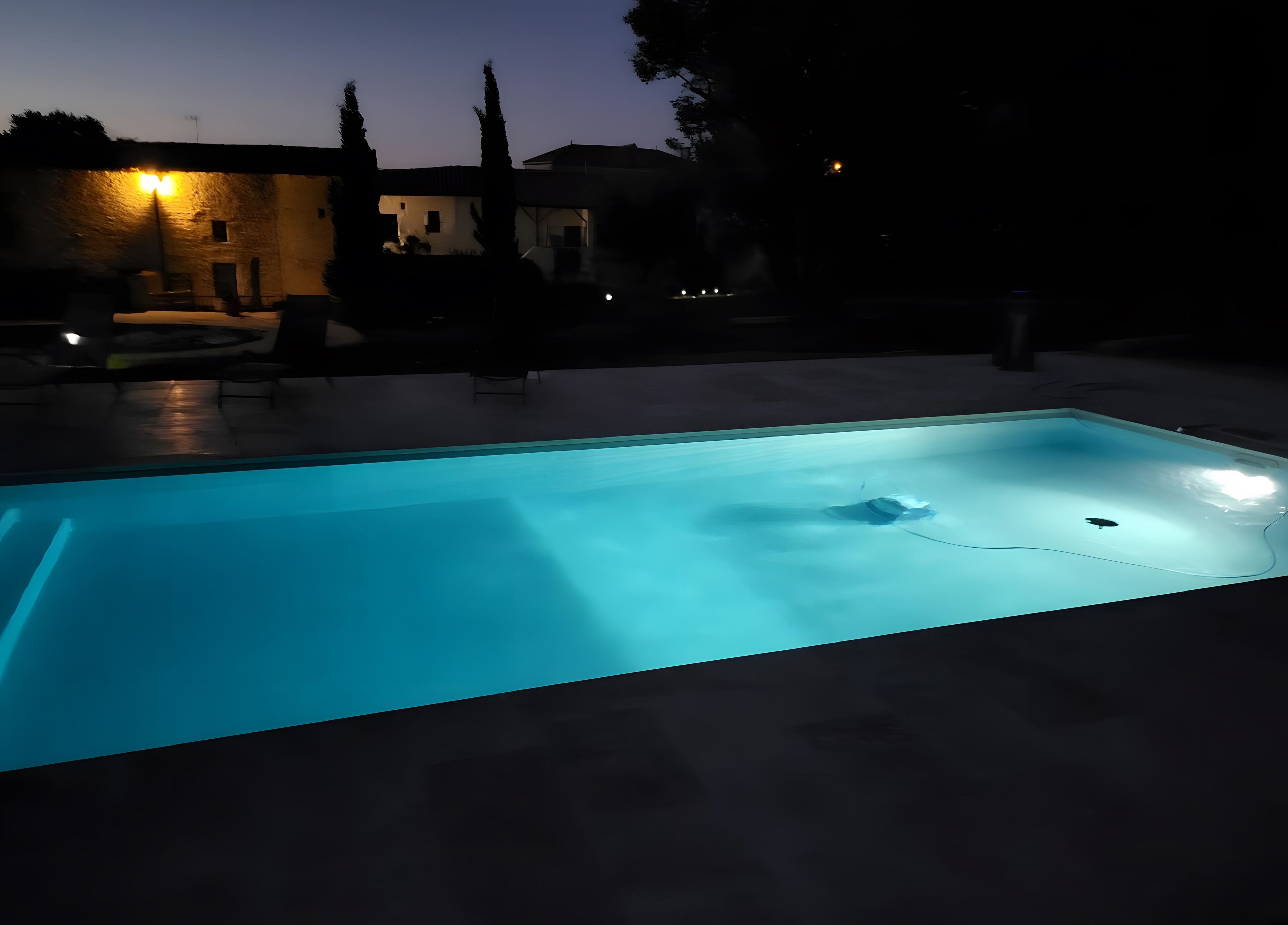 Ein Schwimmbad im Dämmerlicht mit umliegenden Gebäuden und Bäumen.