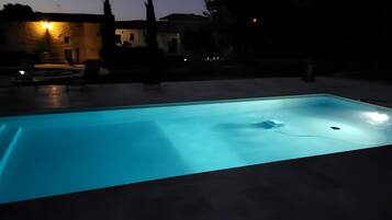 Ein Schwimmbad im Dämmerlicht mit umliegenden Gebäuden und Bäumen.