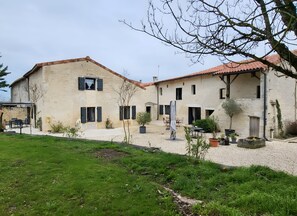 Un bâtiment en pierre de deux étages, avec un toit en tuiles, des places assises à l’extérieur et un espace jardin.