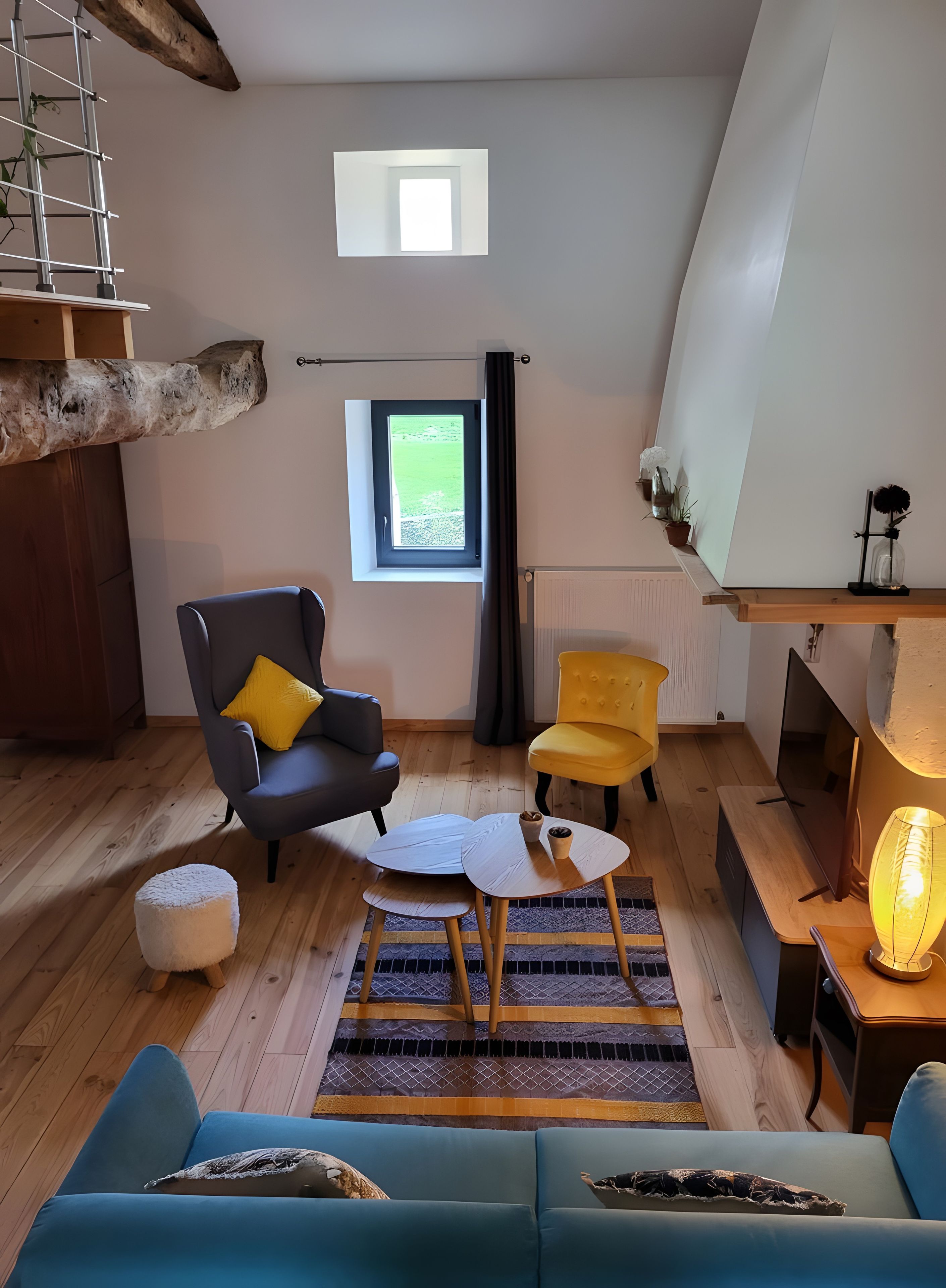 Un salon confortable avec un canapé, des fauteuils, une table basse, un téléviseur et une petite fenêtre donnant sur un beau paysage.