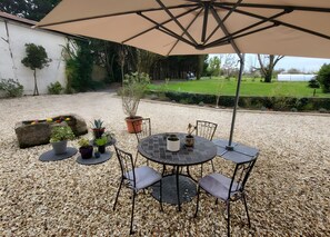 Un espace extérieur aménagé en terrasse, avec une table ronde, des chaises et un grand parasol.