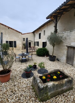 A courtyard with a stone wall, a table with chairs, potted plants, and a flower bed. - Cottage 'Gîte 3 Étoiles Climatisée La Mezza' with Shared Pool, Wi-Fi and Air Conditioning (Mareuil)