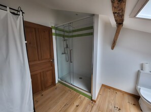 A bathroom with a wooden floor, a glass shower enclosure, a white toilet, and a wooden door. - Cottage 'Gîte 3 Étoiles Climatisée La Mezza' with Shared Pool, Wi-Fi and Air Conditioning (Mareuil)